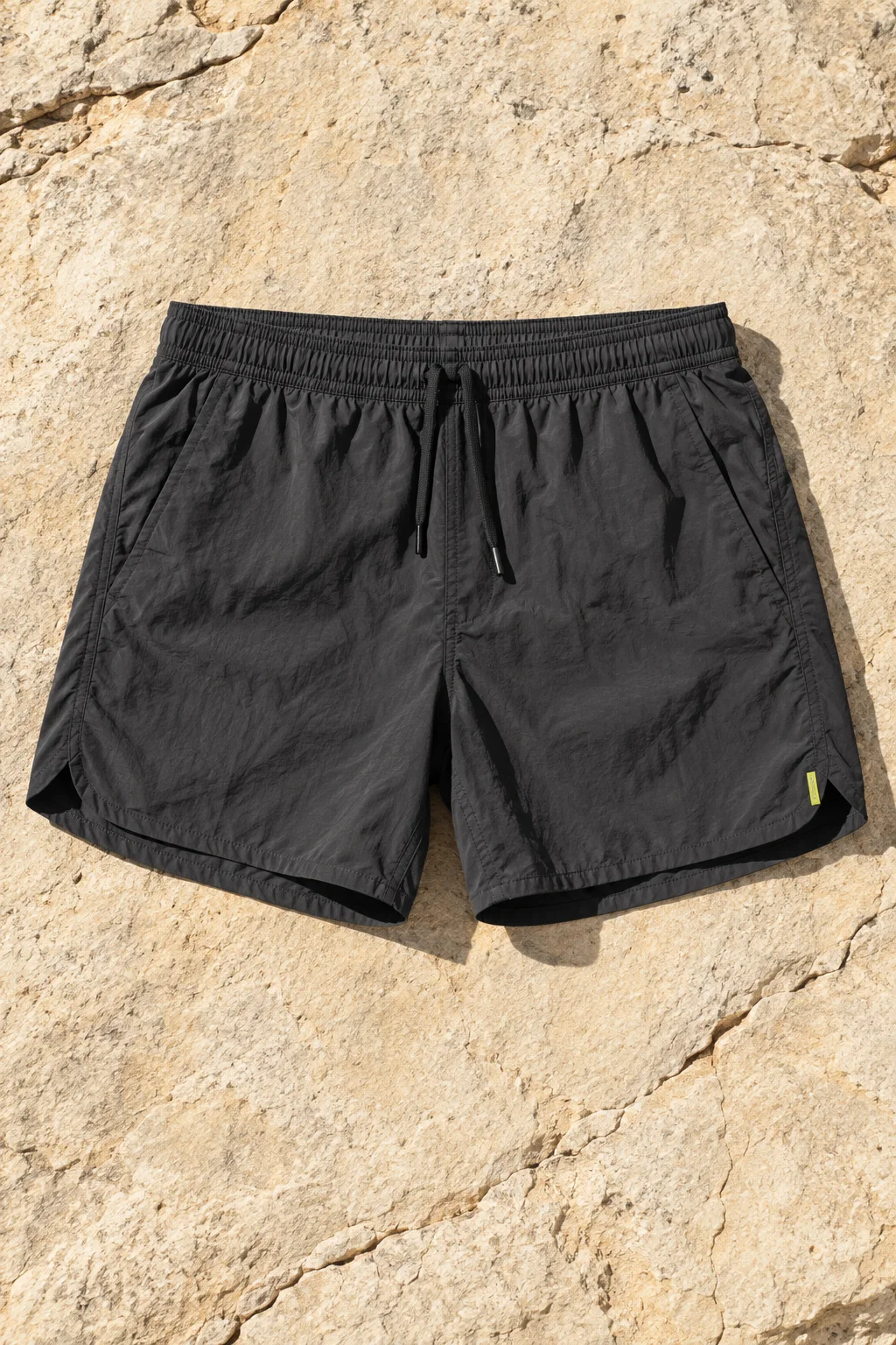 Charcoal five-inch running shorts with a drawcord waist and a small sulphur tab on pale stone